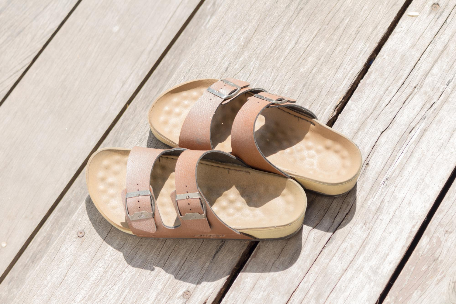 Des sandales en cuir sont posées sur un plancher en bois. 
